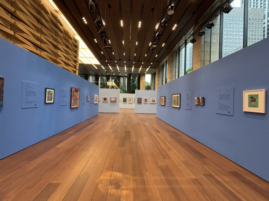 view of a contemporary art gallery. Blue walls with art and descriptions contrast with warm wood tones. Ahead on the left is the illmarks medical chArt 